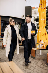 A young couple in love in autumn in outerwear walks on the street and drinks coffee. Recreation in the open air. Young stylish couple.