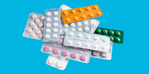 Pile of various pills and tablets in a blister packs on blue background, healthcare and medicine concept