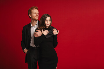 Young couple hugging and looking away while standing isolated over red wall