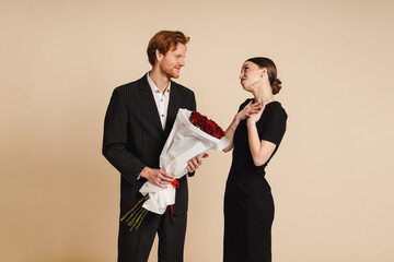 Handsome man giving roses bouquet to his girlfriend isolated over beige wall