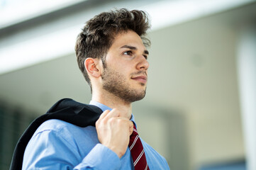 Naklejka premium Young businessman walking and holding his jacket outdoor