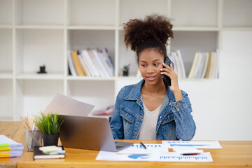 Young African American businesswoman using smartphone and working with pile of documents at office workplace, business finance and accounting concepts.