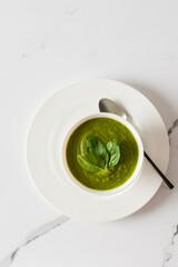 Healthy breakfasts, green broccoli and spinach cream soup in a white bowl on a marble background with a gray napkin, top view