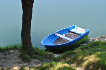 Plastic, blue colored boat in river water, moored to the shore, river bank, with green grass coast
