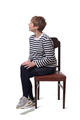 side view full length portrait of a woman in skirt, striped sweater and sneakers sitting on chair  and legs crossed looking away on white background