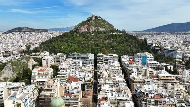 Aerial drone cinematic video of Athens cityscape and iconic chapel of Saint George on top of Lycabettus hill with beautiful deep blue sky, Athens, Attica, Greece