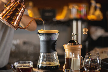 drip coffee, Barista making drip coffee by pouring spills hot water on coffee ground with prepare filter from copper pot to glass transparent chrome drip maker on wooden table in cafe shop