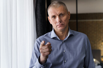 Confident businessman in a blue shirt pointing his index finger at the camera.