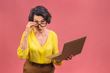 Senior aged business senior mature aged amazed surprised shocked woman with laptop. Grandmother working isolated over pink background.