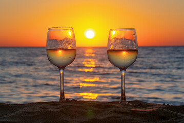 Two glasses of wine on a beach at sunset
