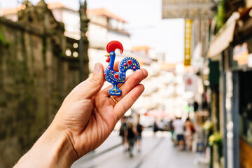 Hand of a man holding a magnet in the shape of a rooster on the street. Porto, Portugal souvenir concept.