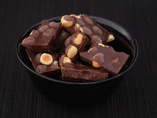 Pieces of broken dark chocolate with hazelnut in a black bowl