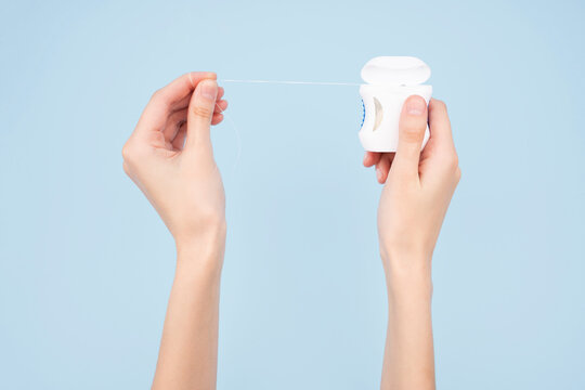Container with dental floss. Dental floss on a blue background. Close up of young female hands holding dental floss on blue background. Dental health care and oral hygiene concept.