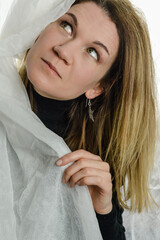 portrait of a beautiful blonde woman who is hiding behind a white fabric and looking up