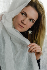 portrait of a beautiful blonde woman who is hiding behind a white fabric and looking to the side