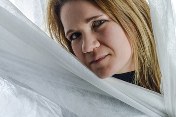 portrait of a beautiful blonde woman sticking her face out of white fabric and hinting a smile