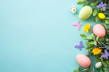 Spring or Easter background on blue. Eggs, spring leaves, flowers and colored butterflies. Flat lay with copy space.