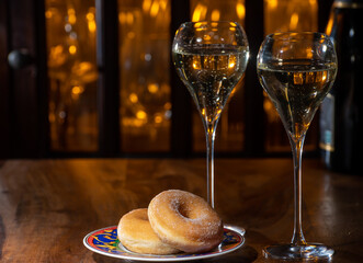 Glass of brut champagne bubbles wine in tulip glass and glazed, yeast-raised, American-style ring doughnut on evening bar lights background