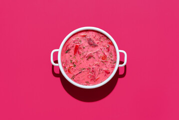 Beetroot soup with sour cream in a white bowl, isolated on magenta background