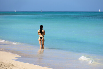 Girl in black bikini going to swim in blue sea water. Beach vacation on Caribbean islands