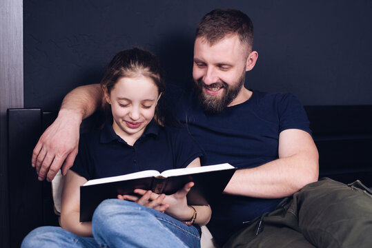 Dad and daughter are reading the Bible book together. Family. A happy child is smiling while sitting on the bed.