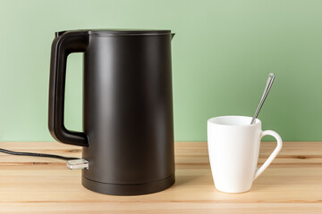 Matte black kettle and white mug on a wooden countertop. Stylish electric kettle for heating water...