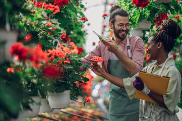 Multiracial couple of gardeners working in a greenhouse and using tablet