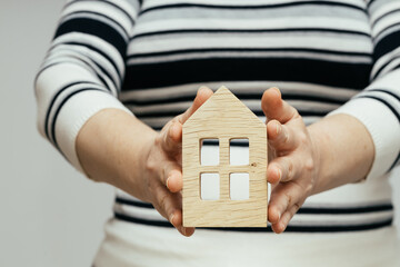 A woman holds a wooden miniature of a house in her hands, Housing concept, building a house, buying an apartment