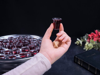 Closeup of young woman taking communion from small cups on black background