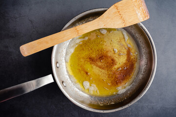 Brown Butter in a Stainless Steel Skillet with a Wooden Spatula: Overhead view of browned butter in a frying pan on a dark background - obrazy, fototapety, plakaty