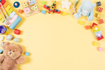 Baby kids toy frame background. Teddy bear, colorful wooden educational, musical, sensory, sorting and stacking toys for children on pastel yellow background. Top view, flat lay
