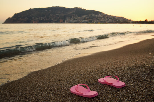 Pink flip flops in sand near the sea at dusk
