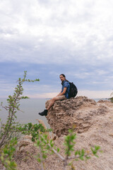 Young Latin man sitting on a rock watching the scenery on a cliff. Vertical photo.