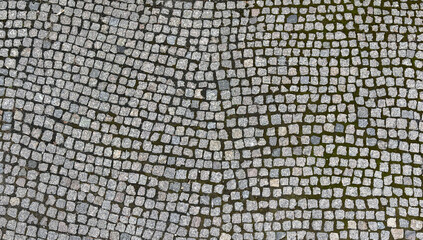 Texture of dark gray granite street paving stones with moss in the seams. Texture or pattern. Street road texture