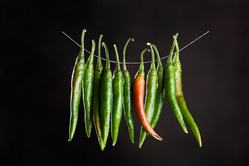 Green chili peppers hanging on a natural rope on a brown background