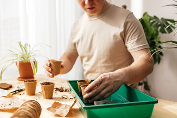 A man puts peat cups in a home greenhouse. Growing vegetables and herbs at home. The garden in the apartment.