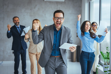 Obraz premium Successful business group celebrating an achievement at the office with arms up and looking at the camera smiling. Shot of a group of young businesspeople huddled together 