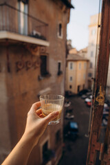 stick out a hand with freshly brewed coffee in the window of an old European street. coffee in a glass cup in a female hand. traditional morning black coffee