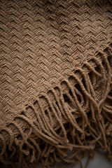 beige woolen plaid from llama wool close-up. knitting details of a woolen plaid with tassels top view.