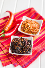 Dry chili pepper flakes. Crushed red peppers in bowl on white table.