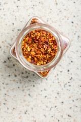 Dry chili pepper flakes. Crushed red peppers in jar on white table. Top view.