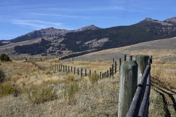 Fototapeta na wymiar American West landscape of farm land fence line, blue sky, and Rocky Mountains
