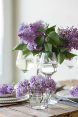 Beautiful table decor for a wedding dinner with a spring blooming lilac flowers. Celebration of a special event. Fancy white plates, wineglasses. Countryside style