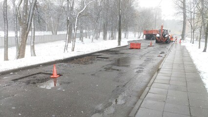 On the wet roadway of the city street, the asphalt pavement is being patching and a tractor and...