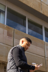 vertical portrait of a latin man in smart casual clothes texting on the street outside her office