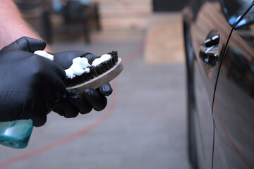 Car cleaning. Brush and cleaner in hand. Foam on the brush. Special means for cleaning the car. Cropped image of a person.Out of focus.