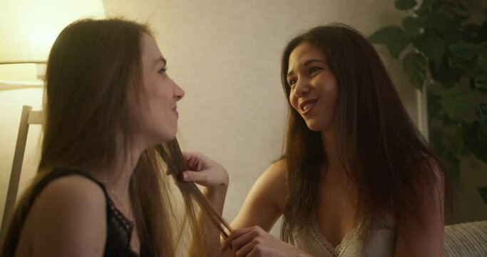 Beautiful young lesbian girlfriends sitting on sofa, touching each other and looking with love
