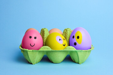 Cute easter eggs with funny faces in green box isolated on light blue background. Happy easter concept. Painted Easter eggs.