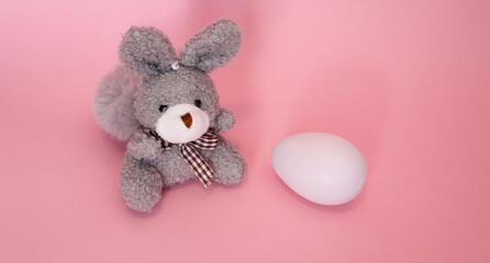 Pequeño y tierno conejo gris de felpa con huevo blanco de plástico. 