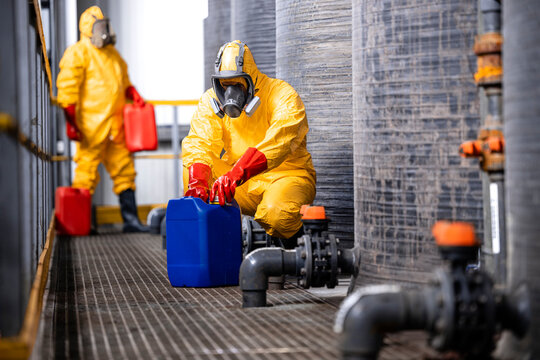 Experienced and protected workers in yellow chemicals suit, gas masks and gloves handling biohazardous waste.